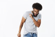 © Cookie Studio - Bearded african american guy showing dance moves as having fun enjoying music, celebrating success and win waving head looking down at feet carefree and cool, posing delighted over gray background
