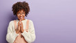 © Wayhome Studio - Smiling dark skinned woman steeples fingers has great plan or intention, wears jumper and overalls, looks curiously away, poses against purple studio wall with free space. Facial expressions.