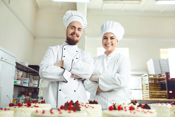 Pastry chefs in white uniform are smiling at bakery.