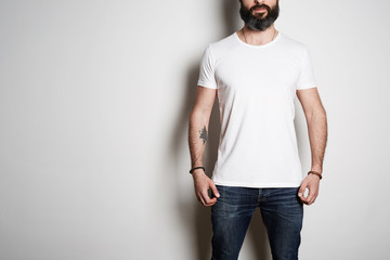 Bearded muscular man model wearing white blank t-shirt with space for your logo or design in casual urban style on the white background. Studio shot.