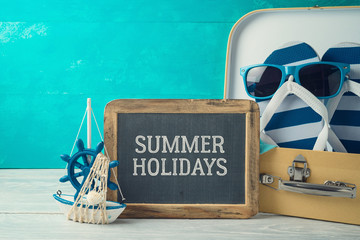 Summer concept background with cute funny flip flops, suitcase and chalkboard sign on wooden table