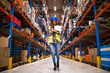 Portrait of confident female worker walking through distribution warehouse. Smiling woman holding checklist.
