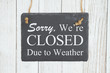 Sorry we're Closed Due to weather text on a hanging chalkboard on weathered whitewash textured wood