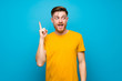 Redhead man over blue wall intending to realizes the solution while lifting a finger up