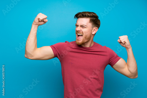 Fotografía Redhead man on isolated blue wall celebrating a victory