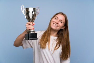 Young woman over blue wall holding a trophy