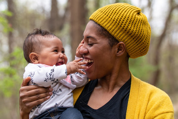 A proud mother with her bew born baby girl in the forest. The baby girl playing with her mothers face while laughing and learning new sensations.