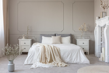 King size bed with white sheets and blanket between two wooden bedside tables flowers in vases