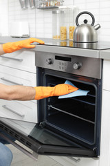 Wall Mural - Young man cleaning oven tray with rag in kitchen