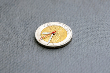 time to benefit: 2 euro coin with hour hands on a dark background, short focus, close