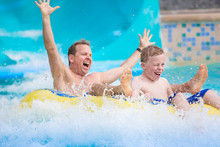 Thrilling Expression Of A Father And His Son As They Splash Down A Water Slide At An Amusement Park During A Summer Vacation. Lifestyle Photo Showing Fun Family Activities