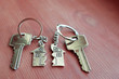 © Inga - Two keys with splitted or broken key rings with pendant in shape of house divided in two parts on wooden background with copy space. Dividing house when divorce, division of property, real estate heri