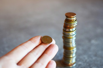 Two cent euro coin in hand next to stock of money coins on grey table with copy space. Personal finance, finance accounting and management, money savings, poverty or thrifty concept.