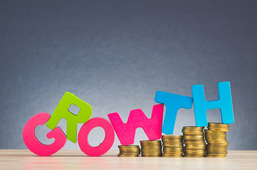 Business success concept, stacking coins and word GROWTH on wooden desk over beautiful reverberation gradient background