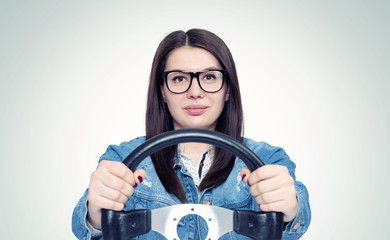 Happy young woman with glasses and car steering wheel, front view, auto concept