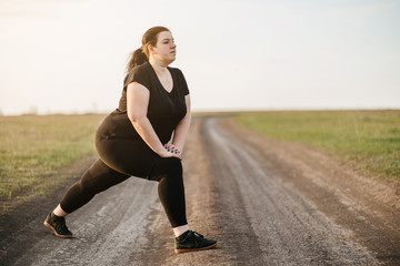 Wall Mural - Cropped portrait of woman in sportswear training legs getting ready for running in the meadow, copy space. Healthy lifestyle, sport, weight losing, activity concept