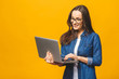 Portrait of a cheerful young woman wearing casual standing isolated over yellow background, holding laptop.