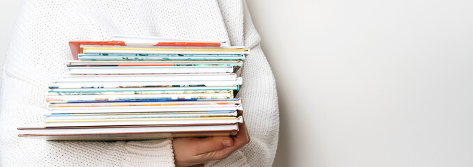 Girl in a white woolen sweater holding a stack of children's books on white background with copy space. Long wide banner