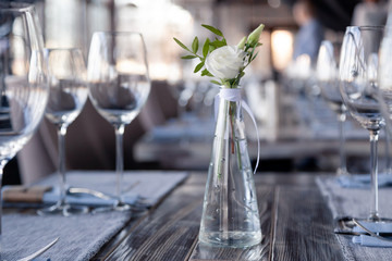 Modern restaurant setting, glass vase with bouquet flowers on table in restaurant. Wine and water glasses stand on wooden table. Concept banquet, birthday, conference, wedding