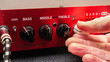 Hand adjusting volume control on a red electric guitar amplifier panel.