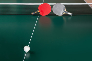 two ping-pong rackets and a ball on a green table.