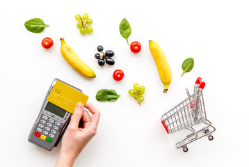 Mobile shopping. Shopping cart, machine for payment with credit card and products on white background top view