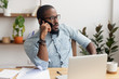 © fizkes - Serious african businessman talking on phone sitting at office desk
