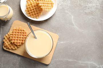 Bowl of condensed milk and waffles served on grey table, top view with space for text. Dairy products