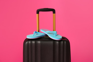 Stylish suitcase with flip flops on color background