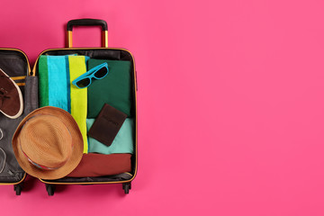 Open suitcase with traveler's belongings on color background, top view. Space for text