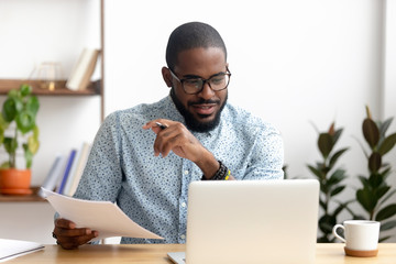 Focused african american businessman working with laptop documents in office