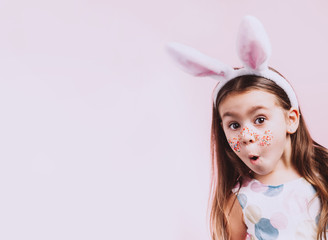 Cute little girl with bunny ears on pink background. Easter child portrait, funny emotions, surprise. Copyspace for text.