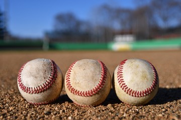 Wall Mural - Photo of three game used baseballs on a baseball infield on a sunny day with a baseball field in the background