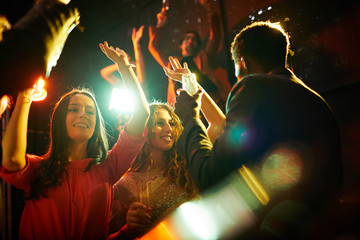 Wall Mural - Happy beautiful girls in stylish blouses drinking champagne and dancing at party in nightclub