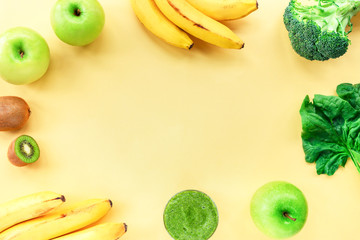 Glass of green smoothie and ingredients for it: banana, apple, spinach, kiwi, broccoli on the yellow background. Top view, copy space.