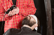 © malkovkosta - Barber work with clipper machine in barbershop. Professional trimmer tool cuts beard and hair of young guy in barber shop salon.