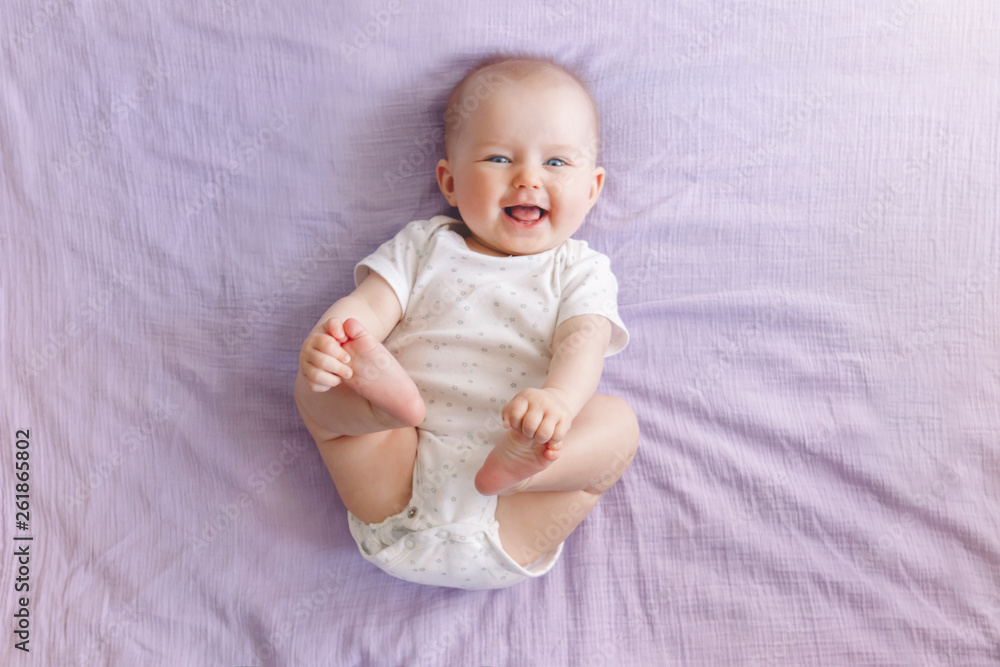 Portrait of cute adorable smiling laughing white Caucasian baby girl boy with blue eyes four months old lying on bed looking at camera. View from top above. Happy childhood lifestyle. - obrazy, fototapety, plakaty 
