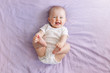 Leinwandbild Motiv Portrait of cute adorable smiling laughing white Caucasian baby girl boy with blue eyes four months old lying on bed looking at camera. View from top above. Happy childhood lifestyle.