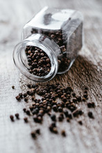 Black Pepper Is Poured From A Glass Jar On A Wooden Surface
