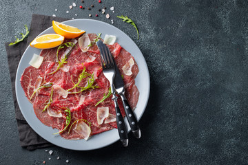 Marbled beef carpaccio with arugula, lemon and parmesan cheese on dark concrete table. Top view, flat lay with copy space