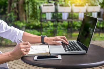 Man working on modern laptop sitting outside natural hardwood desk with green flora background sunlight day outdoor, everywhere you are from laptop concept.