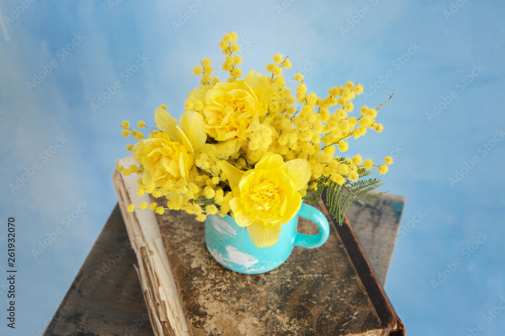 Cup with beautiful yellow flowers and old book on color background