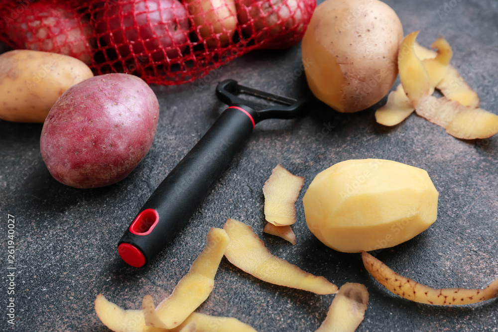 Raw potatoes with peeler on grey background