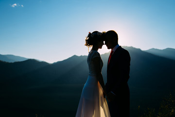happy wedding couple staying and kissing over the beautiful landscape with mountains during sunset