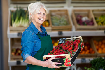 Shop assistant holding box with fresh strawberries in organic produce shop