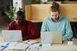 © Seventyfour - Portrait of two contemporary business using laptops sitting at desk and while working in office