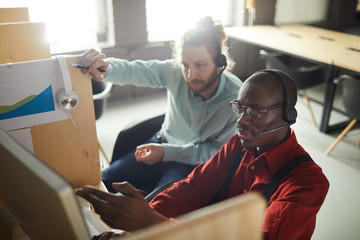 Portrait of African-American hotline operator pointing at computer screen while working with colleague in cubicles, copy space