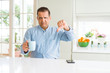 © Krakenimages.com - Middle age business man drinking coffee in the morning at home with angry face, negative sign showing dislike with thumbs down, rejection concept