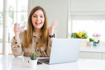 Wall Mural - Beautiful young woman working with computer takes a break to drink glass of water very happy and excited, winner expression celebrating victory screaming with big smile and raised hands