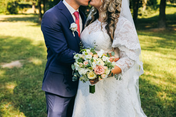 Wall Mural - Wedding couple walking in the green park. Curvy bride in white lace dress and groom are holding hands. Overweight happy people. Love story outdoors. Beautiful bouquet.